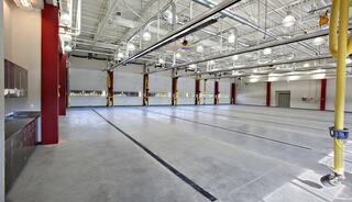 A spacious, well-lit industrial area with concrete flooring, high ceilings, and multiple overhead lights, featuring red columns and utility hooks.