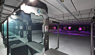 A modern shooting range features several individual lanes with high-tech equipment, ambient lighting, and a spacious, sleek design.