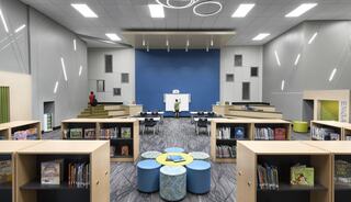 A modern library space features bookshelves, colorful seating, and a presentation area, encouraging reading and collaboration among visitors.