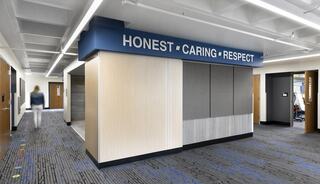 A modern hallway features a wall with the words "HONEST, CARING, RESPECT" prominently displayed, emphasizing a positive environment.