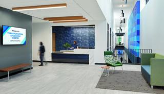 A modern building features large windows, surrounded by greenery, with a well-paved parking lot under a colorful sunset sky.