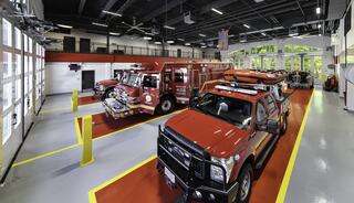 A modern fire station featuring red emergency vehicles, bright lighting, and spacious garage areas with clear windows.