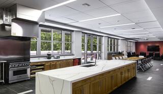 A spacious, modern kitchen featuring a large white marble island, wood cabinetry, stainless steel appliances, and ample natural light.