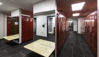 A modern locker room features red lockers, wooden benches, and tiled flooring, with bright overhead lights enhancing the clean atmosphere.