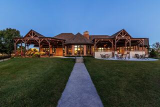 A spacious, beautifully lit lodge with a large lawn, wrapped in wooden beams and inviting outdoor seating, perfect for gatherings.