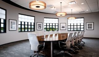 A modern conference room features a large oval table, stylish chairs, and large windows, with framed pictures adorning the walls.