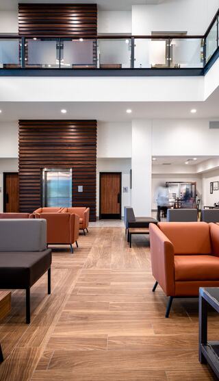 A modern lobby features stylish seating, warm wood flooring, and a bright, open layout with large windows and upscale finishes.
