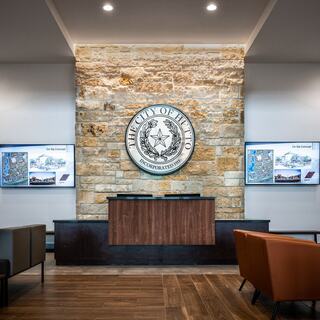 A welcoming lobby features a stone wall with a city seal, flanked by digital displays and modern seating, creating a professional environment.