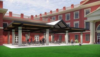 A modern outdoor pavilion sits on lush green grass next to a classic brick building, showcasing a blend of contemporary and traditional architecture.