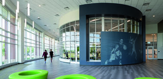 A spacious, modern recreation center features large windows, green seating, and a wall mural depicting athletes, creating an energetic atmosphere.
