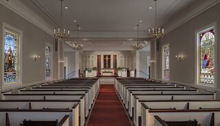 A serene church interior features wooden pews, vibrant stained glass windows, and a simple altar, illuminated by soft lighting.