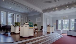 A serene, modern space features a raised platform with podiums, large windows, and elegant decor, ideal for gatherings or ceremonies.