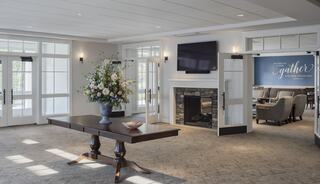 A welcoming lobby features a large table with decorative flowers, a fireplace, and seating areas, exuding warmth and comfort.