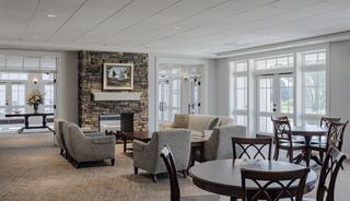 A cozy, modern lounge features comfortable seating, a stone fireplace, and large windows offering a bright and welcoming atmosphere.