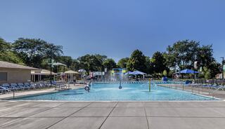 A sunny, inviting pool area features clear blue water, lounge chairs, umbrellas, and surrounding greenery, perfect for relaxation and fun.