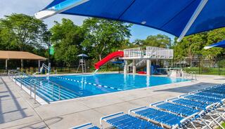A vibrant pool area features a water slide, shaded seating, and lush greenery, perfect for a fun day in the sun.