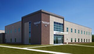A modern, multi-story building features large windows and a welcoming entrance, set against a clear blue sky and green grass.