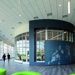 A spacious, modern recreation center features large windows, green seating, and a wall mural depicting athletes, creating an energetic atmosphere.
