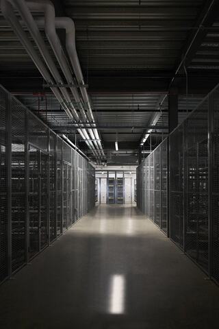 A dimly lit corridor lined with metal racks and pipes overhead, leading to a secured entry, creates a high-tech, industrial atmosphere.
