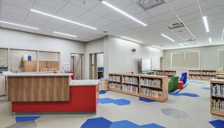 A modern library space features colorful furniture, book shelves, and bright lighting, creating an inviting atmosphere for reading and learning.