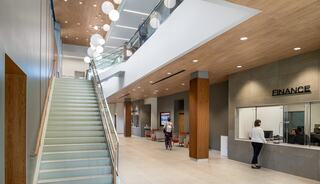 A modern, spacious lobby features a staircase, elegant lighting, and a finance office, creating a welcoming atmosphere for visitors.