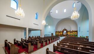 A spacious, modern church interior features wooden pews, vibrant iconostasis, and elegant chandeliers, creating a tranquil atmosphere.