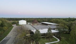 A tranquil landscape features a large building complex with a distinct dome structure, surrounded by greenery and a serene evening sky.