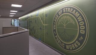 A modern office space features a large mural displaying a map alongside a logo for the Village of Streamwood Public Works.