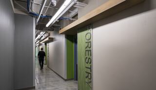 A person walks down a modern corridor with green accents, featuring a sign for "Forestry" on one of the doors.