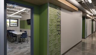 A modern hallway features a well-lit meeting room with a table and chairs, accented by green walls and unique wave patterns.