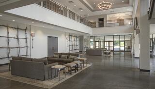 A spacious, modern lobby features sleek furniture, high ceilings, large windows, and stylish decor elements for an inviting atmosphere.