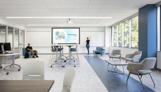 A modern learning space with collaborative seating, a large screen displaying content, and a student engaged in writing on a whiteboard.
