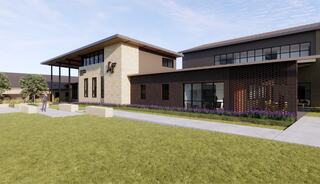 A modern building with a mix of stone and wood features, surrounded by greenery and purple flowers, creating a welcoming architectural space.