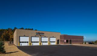A modern fire station featuring multiple garage doors, set against a clear blue sky and surrounded by trees, showcasing a neat, paved area.