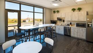 A modern kitchen features a large island, bar stools, a dining table, and ample natural light from large windows.
