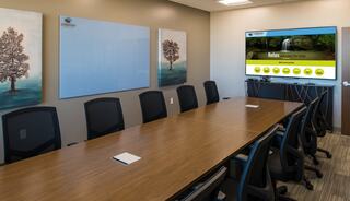 A sleek conference room features a long wooden table, black chairs, and a large screen displaying soothing imagery and options.