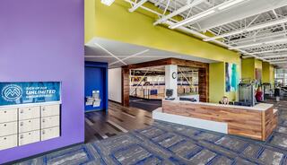 A modern reception area features colorful walls, a check-in desk, lockers, and fitness equipment in a spacious, well-lit environment.