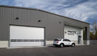 A modern metal building features a large garage door and a vehicle parked outside, with signage indicating it's a county maintenance facility.
