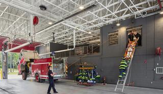Firefighters training with a ladder and rescue equipment inside a fire station, showcasing teamwork and emergency preparedness.