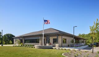 A modern brick building with a flagpole, surrounded by well-maintained landscaping and clear blue skies, suggesting a welcoming environment.