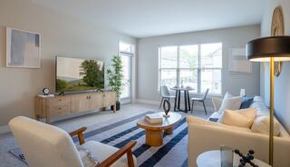 A cozy living room with a large TV, a comfortable sofa, modern decor, a circular coffee table, and bright natural light from ample windows.
