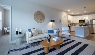 A modern living space featuring a light-colored sofa, stylish decor, and an open kitchen with sleek appliances, all accented by a striped rug.