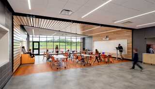 A modern classroom features students at desks, large windows with natural light, and a welcoming, open layout with wooden accents.