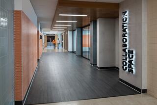 A modern hallway features a "COLLABORATION SPACE" sign, sleek surfaces, and a vibrant color scheme, with people walking in the distance.