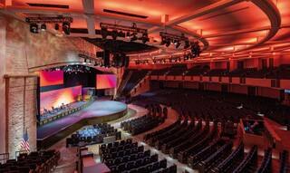 A spacious auditorium with a circular stage, vibrant lighting, and rows of seating, perfect for performances and events.