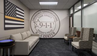 A modern waiting area features a flag, a large 9-1-1 center emblem, and comfortable seating, emphasizing emergency communication services.