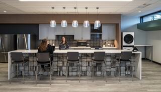 A modern kitchen features sleek countertops, stylish bar stools, and pendant lighting, with two women engaged in conversation.