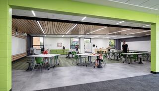 A modern classroom with vibrant green accents, featuring flexible desks, large windows, and students engaged in activities.