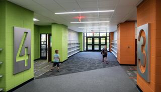 A brightly colored hallway features children walking by large numerals, with shelves lining the walls, creating an inviting atmosphere.