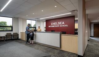 A welcoming school reception area features a desk, friendly staff, and students, highlighting a modern educational environment.